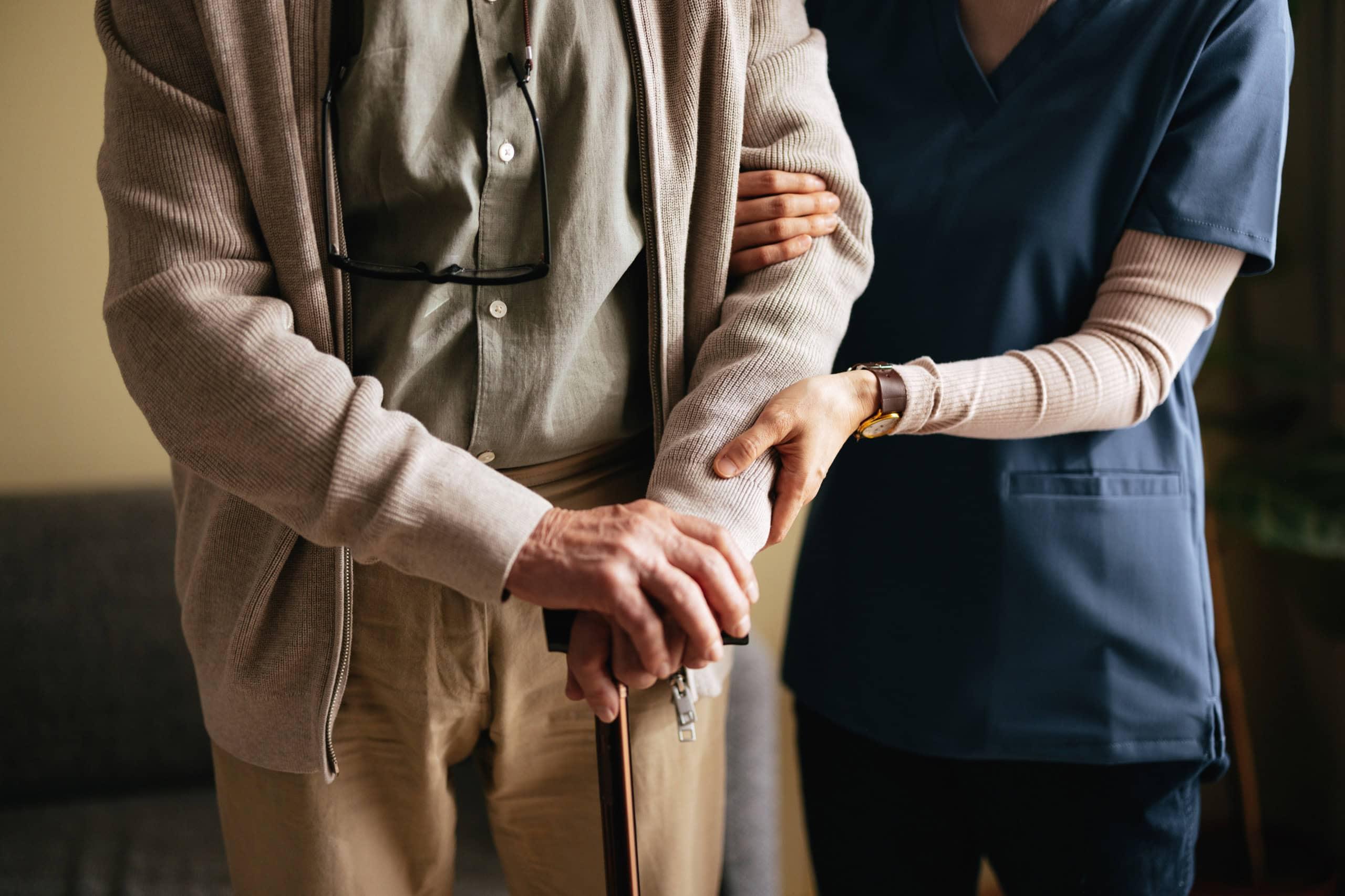 A professional providing assistance to an elderly person, demonstrating support in an aged care setting with a focus on patient care.