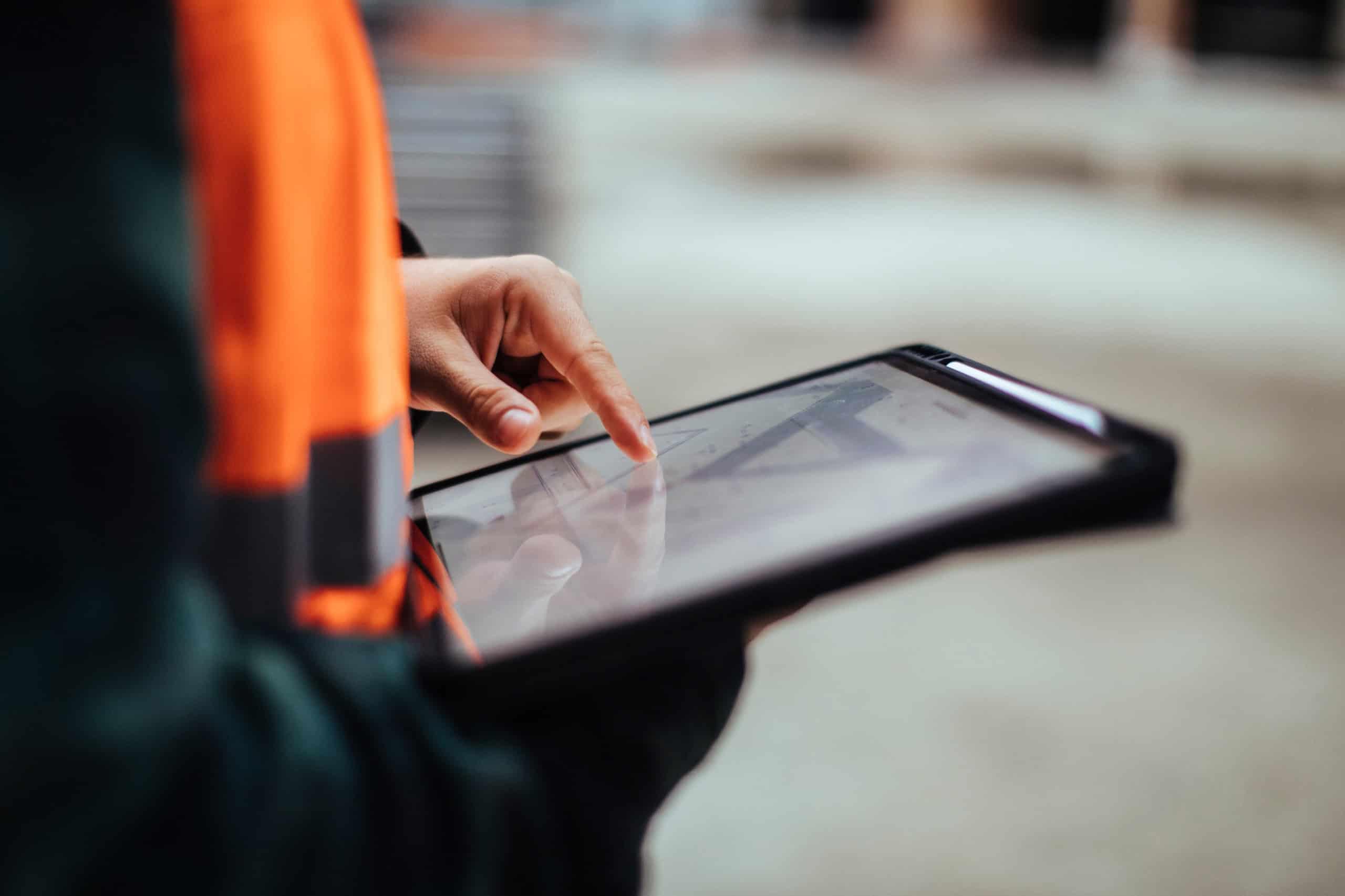 A construction worker wearing a safety vest and helmet is looking at a tablet, managing project-related tasks, showcasing project management in action.