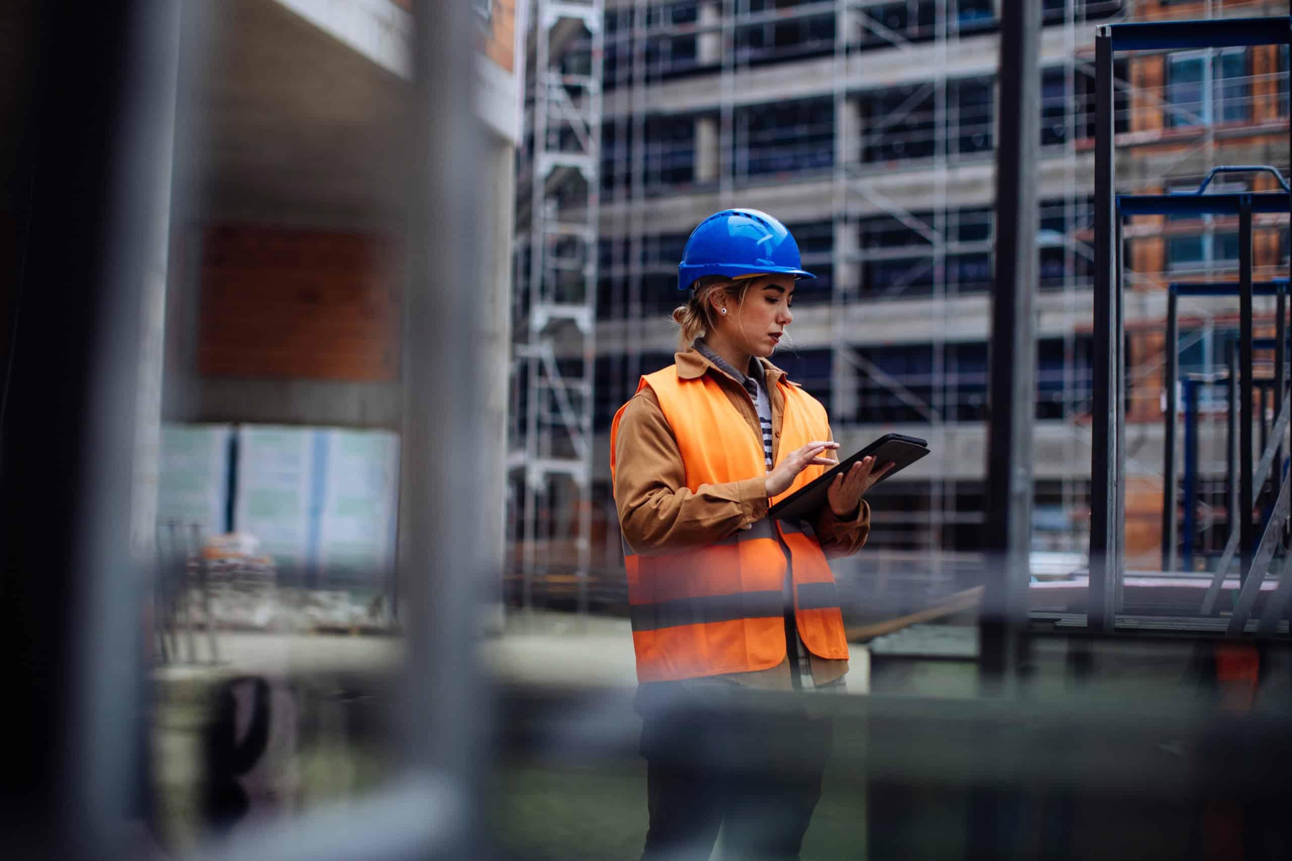 A professional wearing a hard hat and safety vest, standing in front of machinery, engaged in asset management tasks, possibly inspecting equipment.