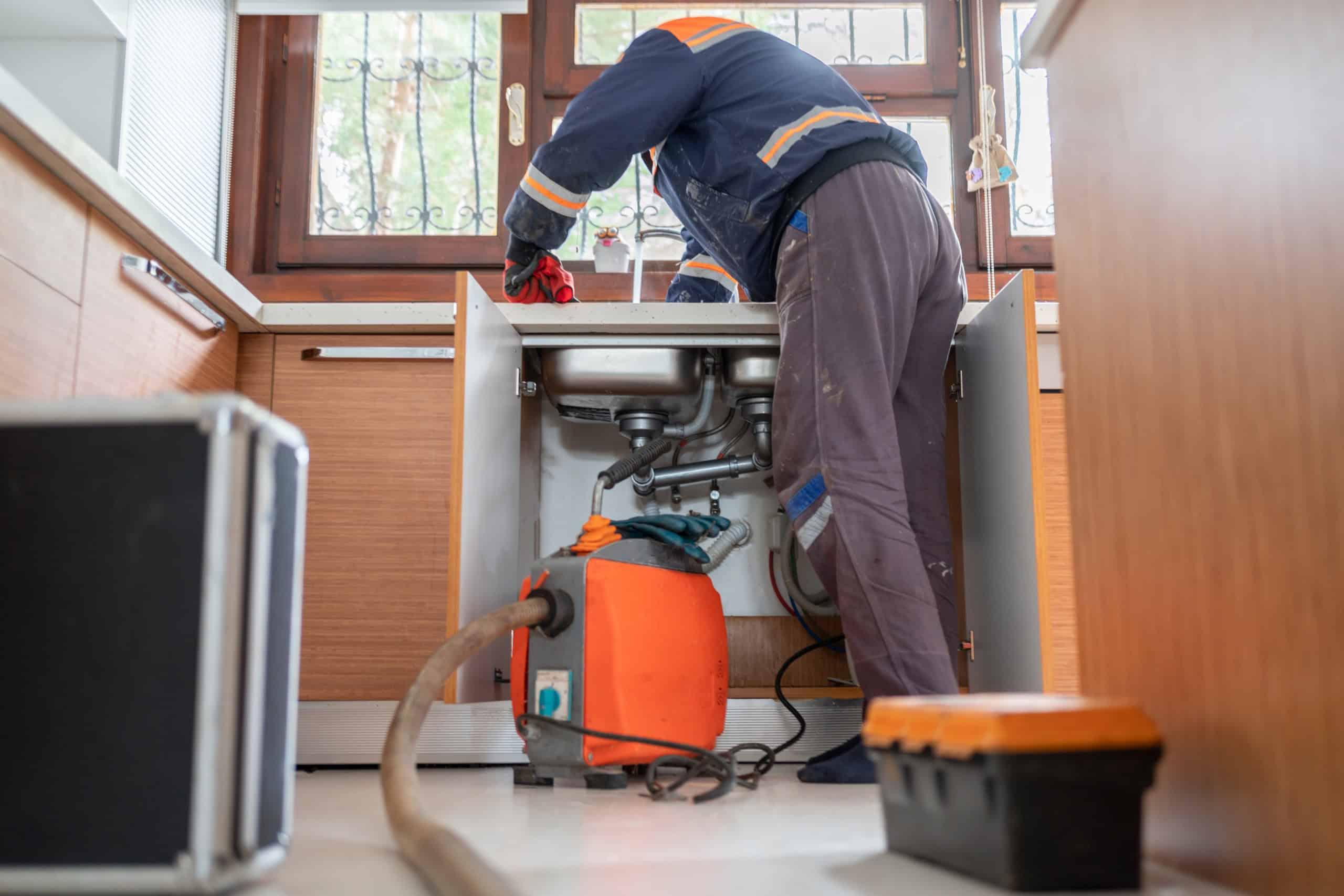 A worker in work boots and a safety vest is setting up or maintaining equipment in an indoor wet space, reflecting the hands-on aspect of facilities management.