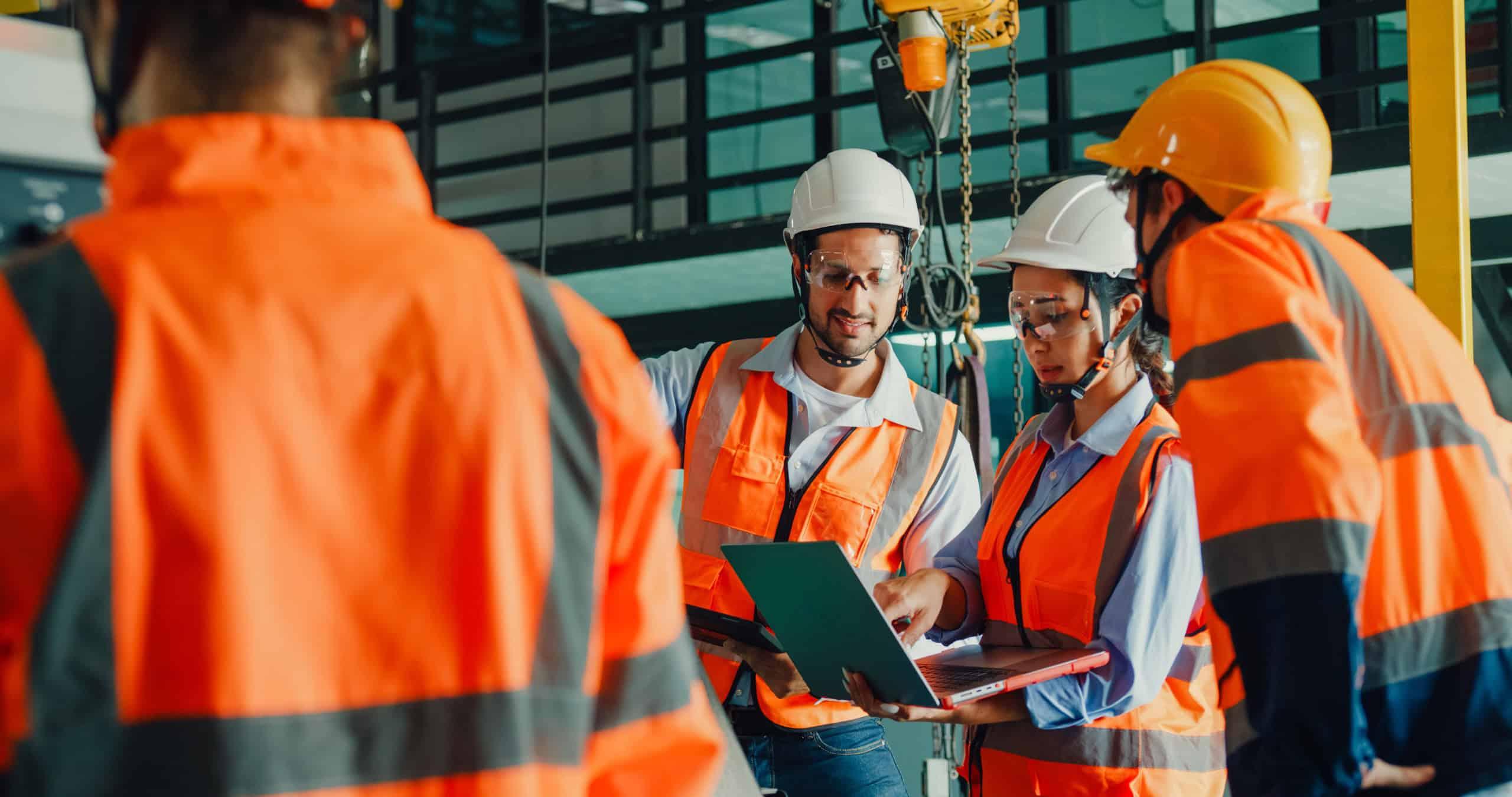 Construction team in high-visibility gear reviewing plans on-site, emphasizing teamwork, compliance, and safety in project-based facilities management.
