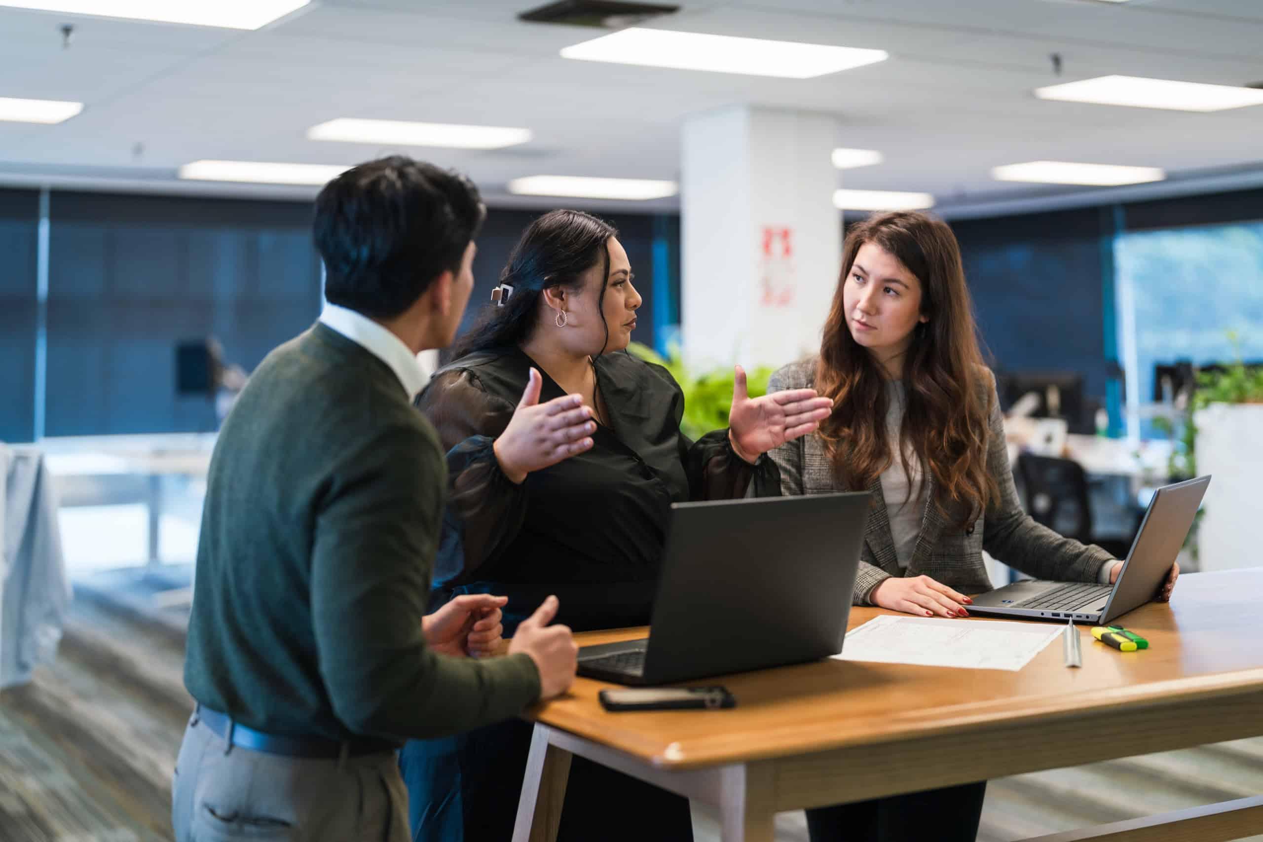 Coworkers having a discussion around a standing desk, highlighting collaborative office design and flexible workspace management.