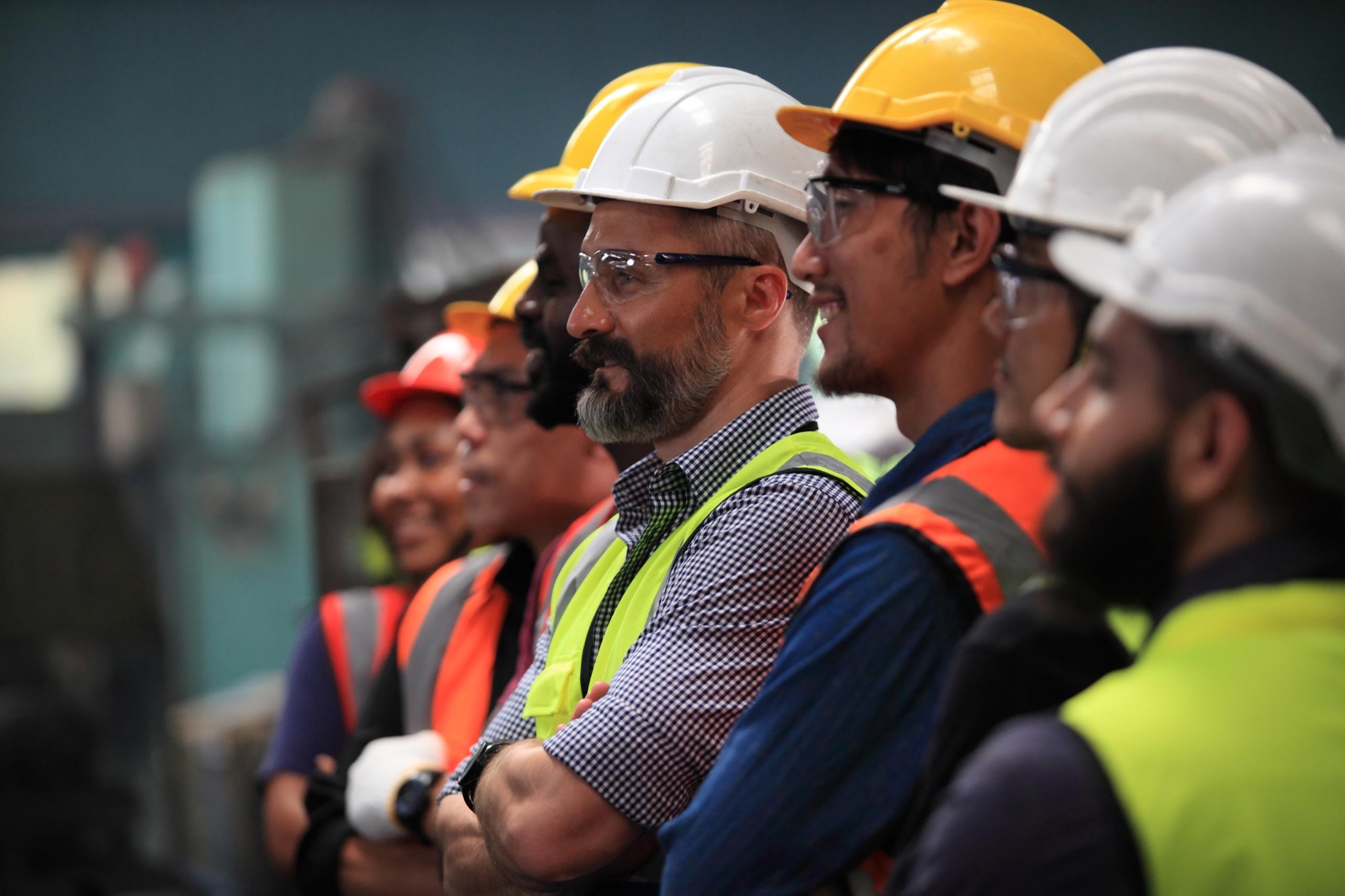 A group of construction or facilities maintenance workers in hard hats and safety gear, standing together and smiling, conveying teamwork and professionalism.